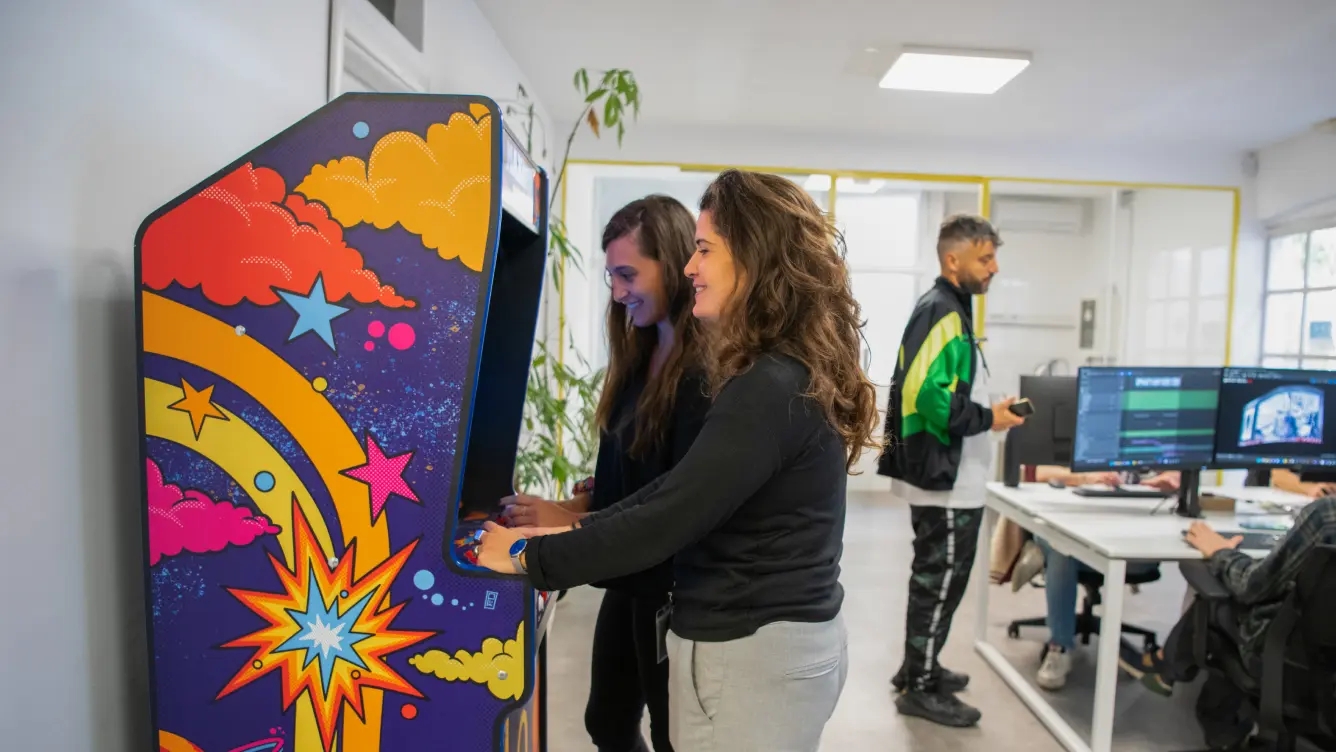 Centounopercento's workplace with girls playing coin-operated games and a boy conversing with colleagues